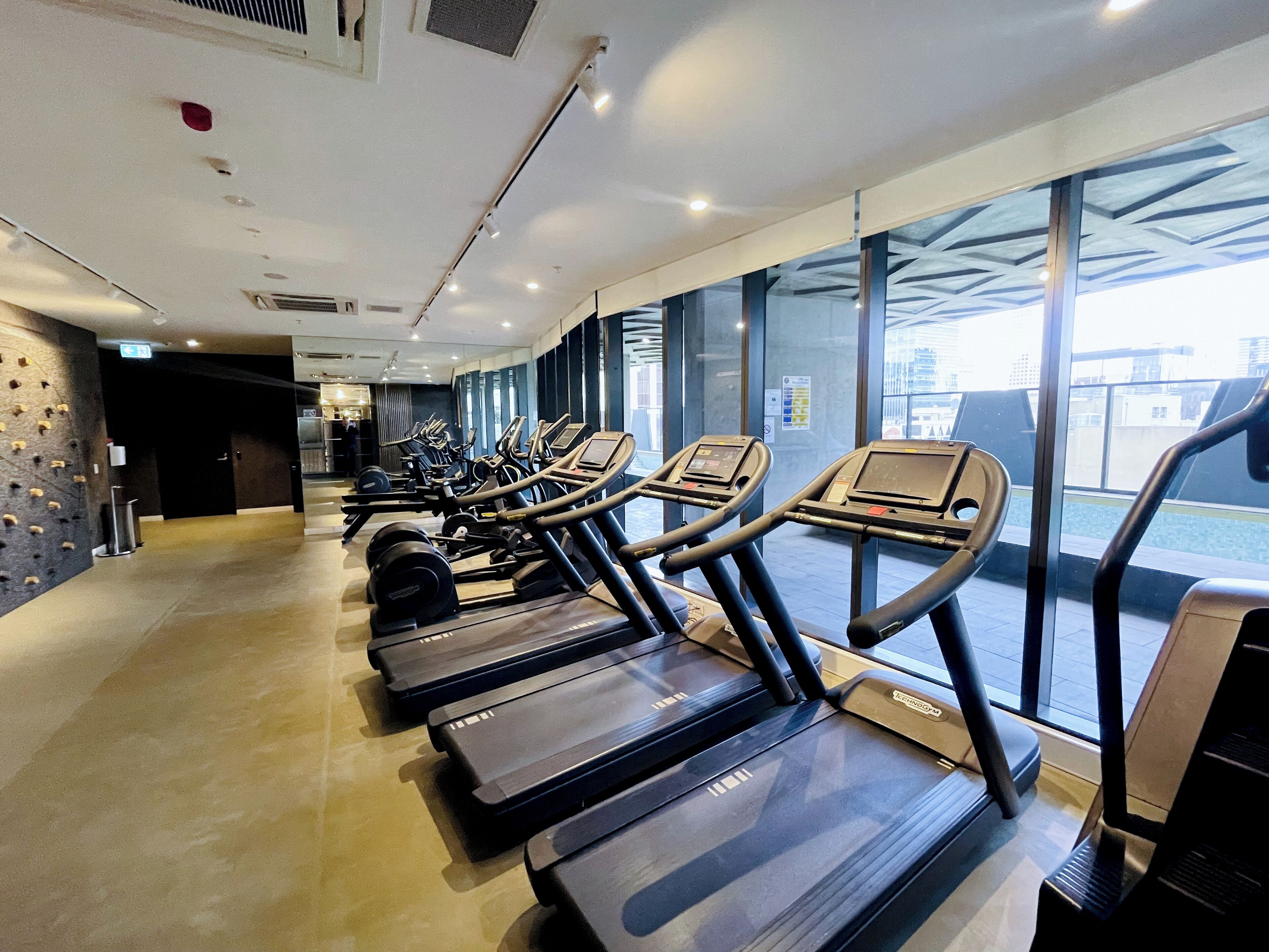 Un gimnasio con cintas de correr, máquinas de pesas y una pared para escalada.