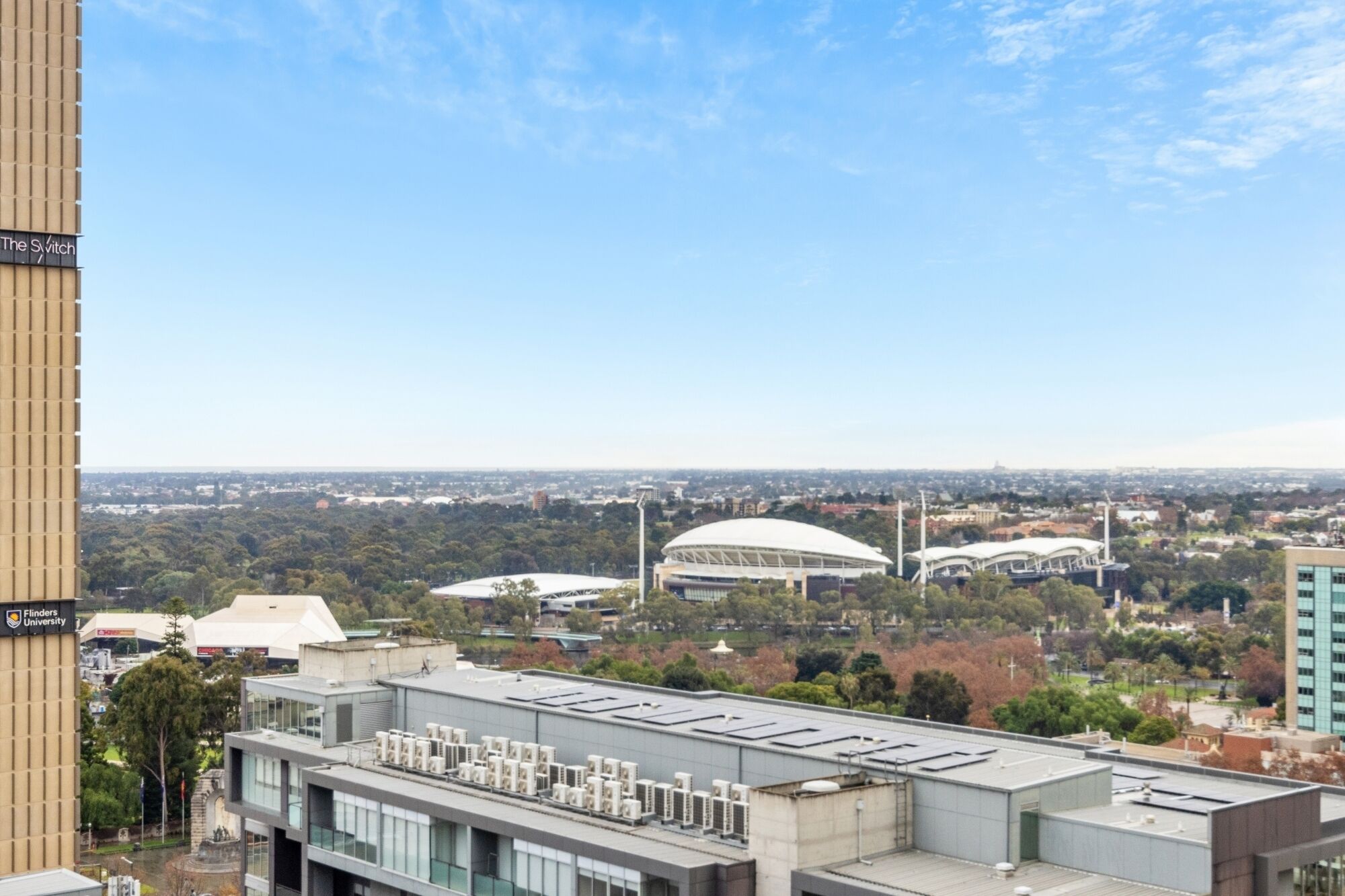 Une vue sur un paysage urbain comprenant un stade, des bâtiments universitaires et un immeuble moderne doté de climatiseurs.
