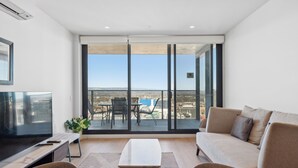 Una sala de estar moderna con un televisor grande, un sofá, una mesa de centro y un balcón con vistas a la ciudad.