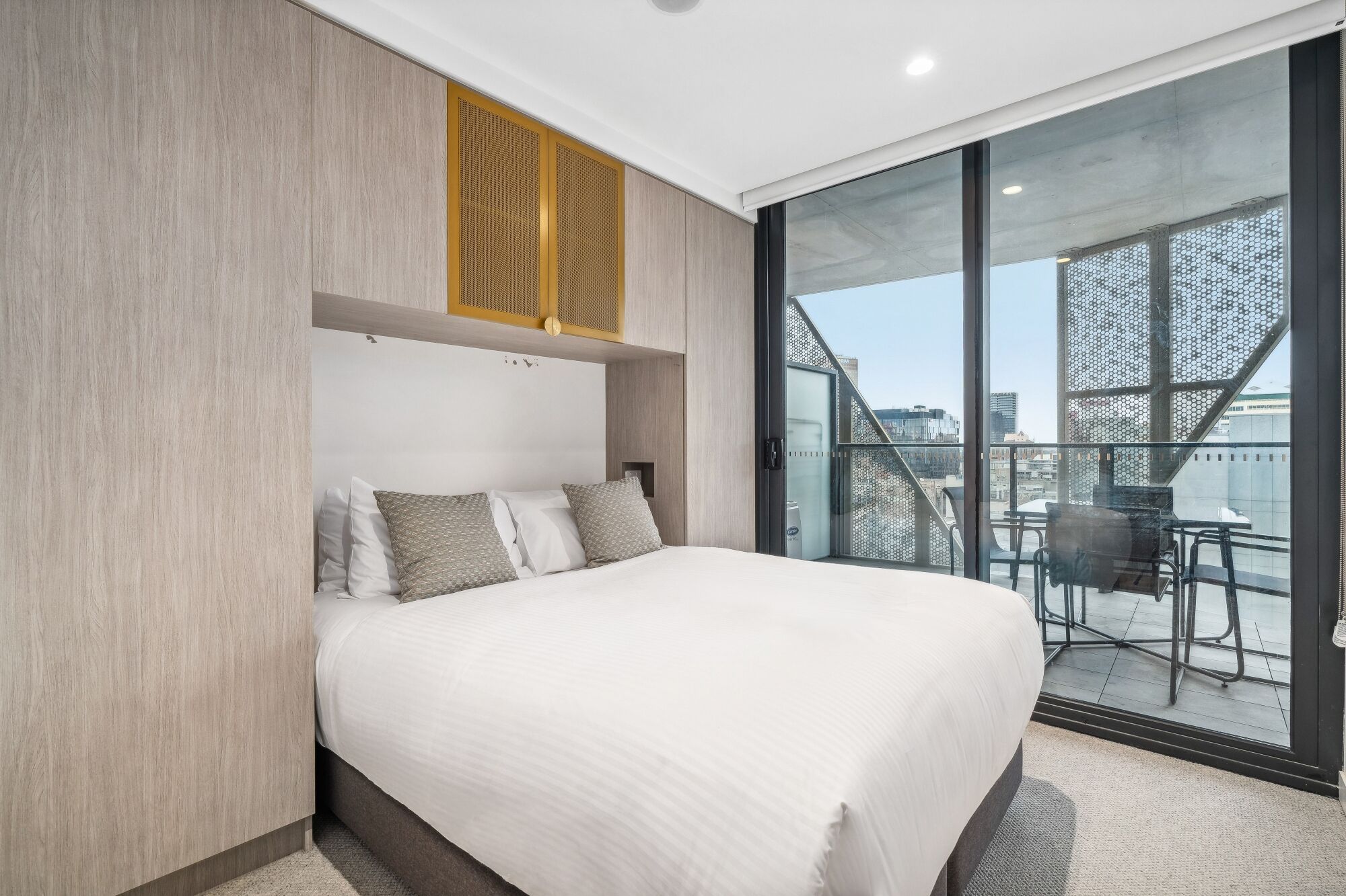 Een hotelkamer met een groot bed, een schuifglazen deur naar een balkon en uitzicht op de stad.