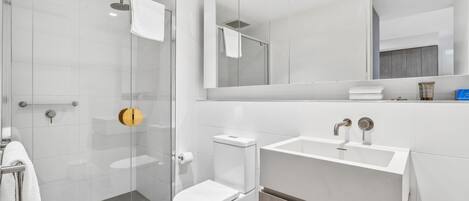 A modern bathroom with a glass-enclosed shower, a white toilet, and a vanity with a mirror.