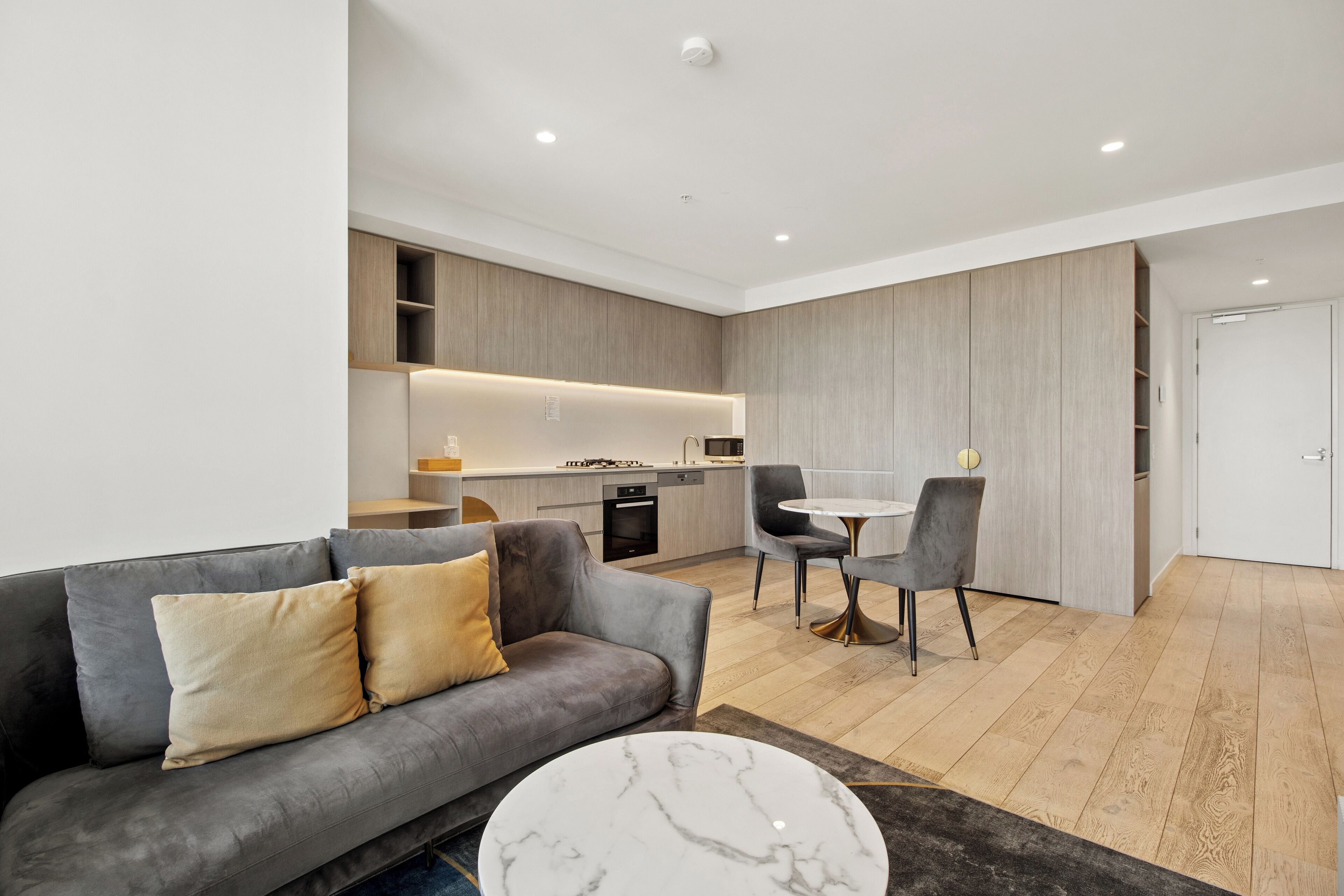 A modern living room with a grey sofa, a marble coffee table, and a kitchen in the background.
