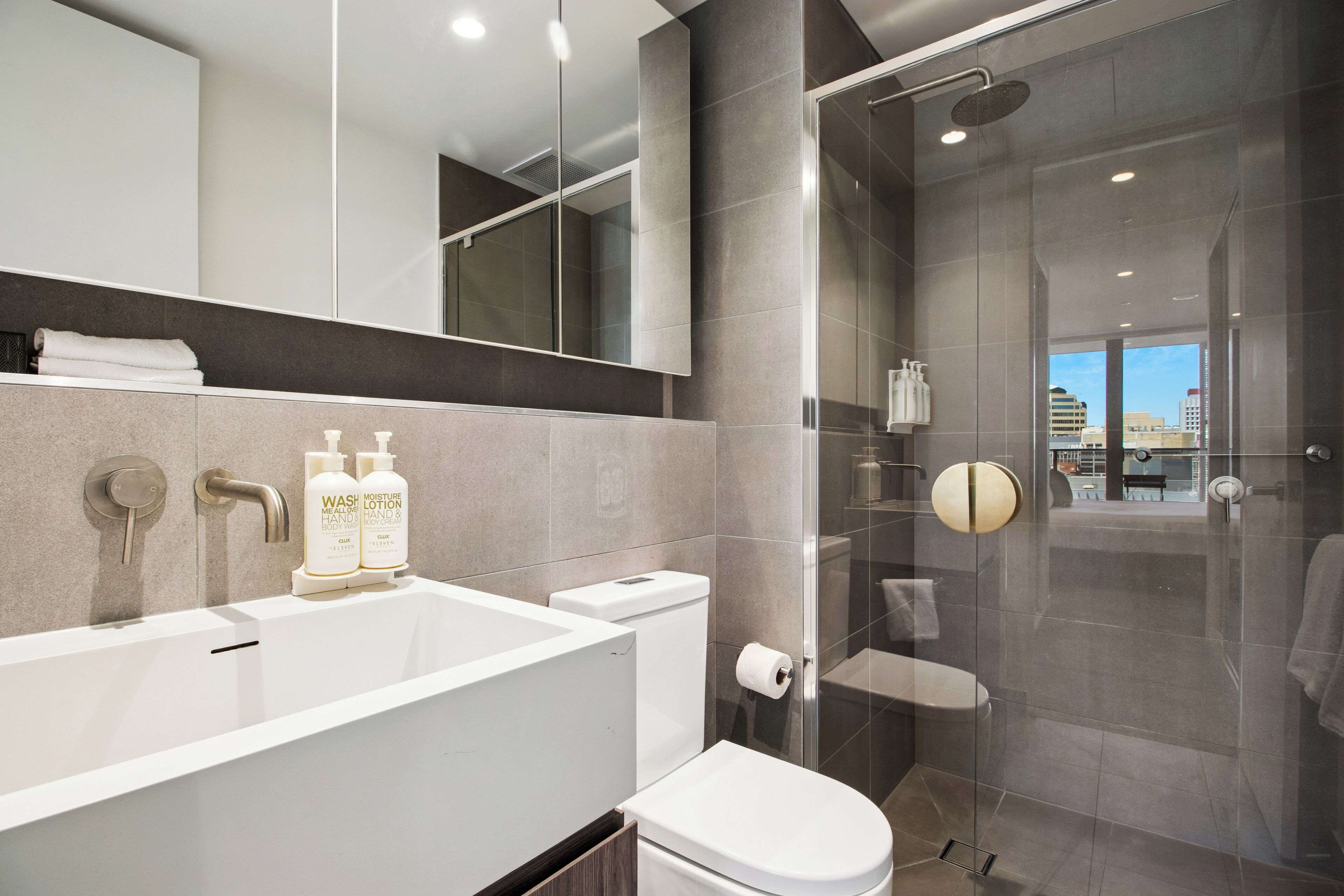 Un baño moderno con una bañera grande, un inodoro, una ducha con mampara de cristal y un espejo sobre el lavabo.