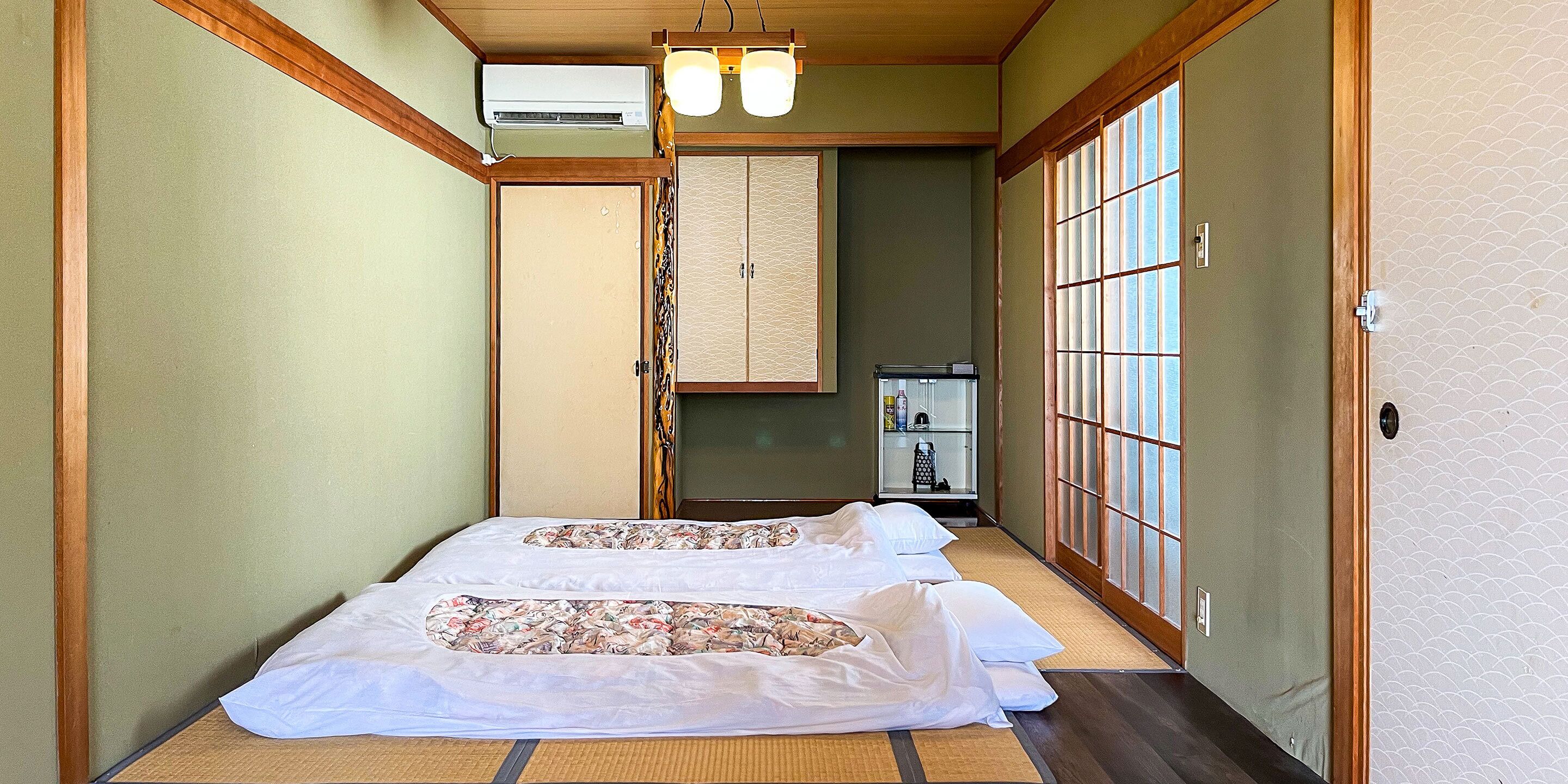 A traditional Japanese room with tatami flooring, two beds with floral bedding, a sliding door, and a small cabinet with toiletries.