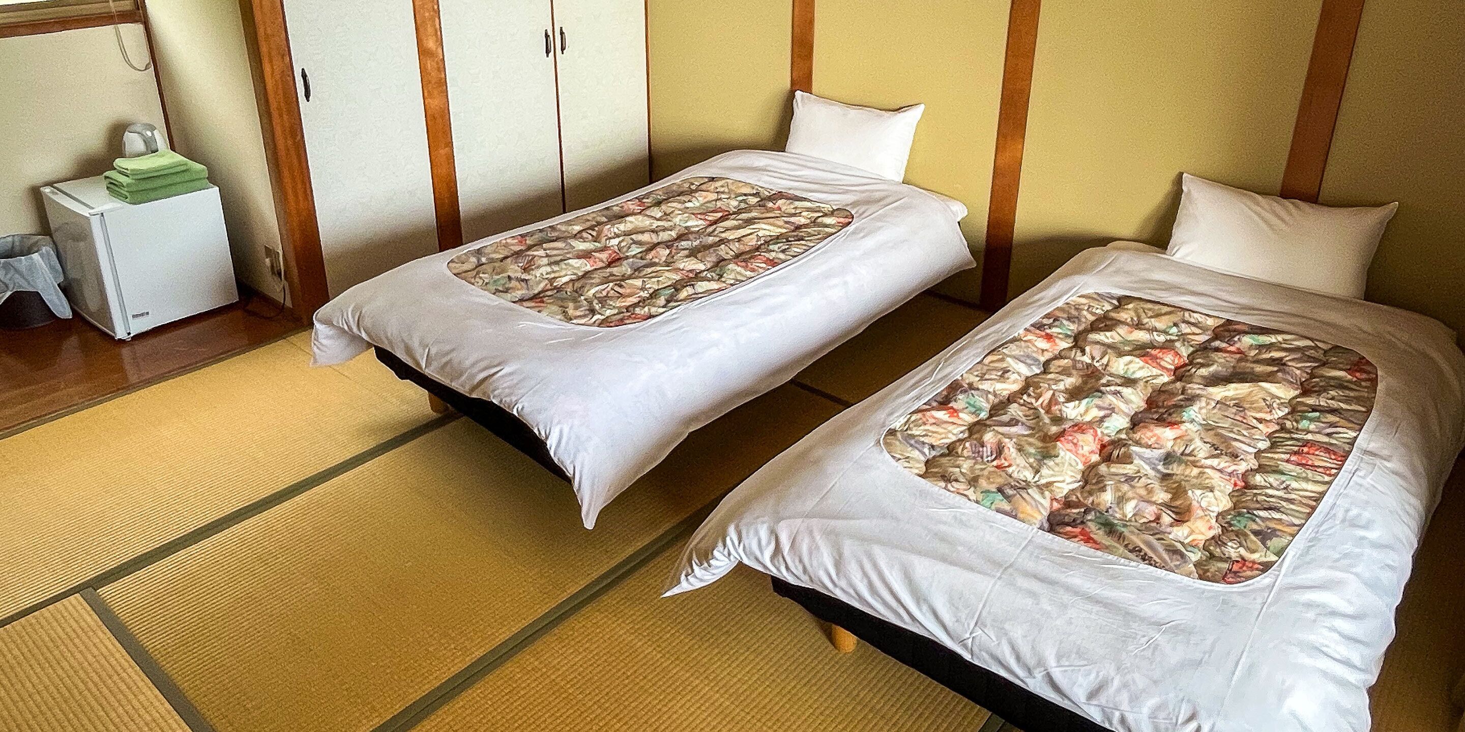 Dos camas individuales con ropa de cama estampada en una habitación con paneles de madera y un escritorio pequeño con un objeto verde encima.