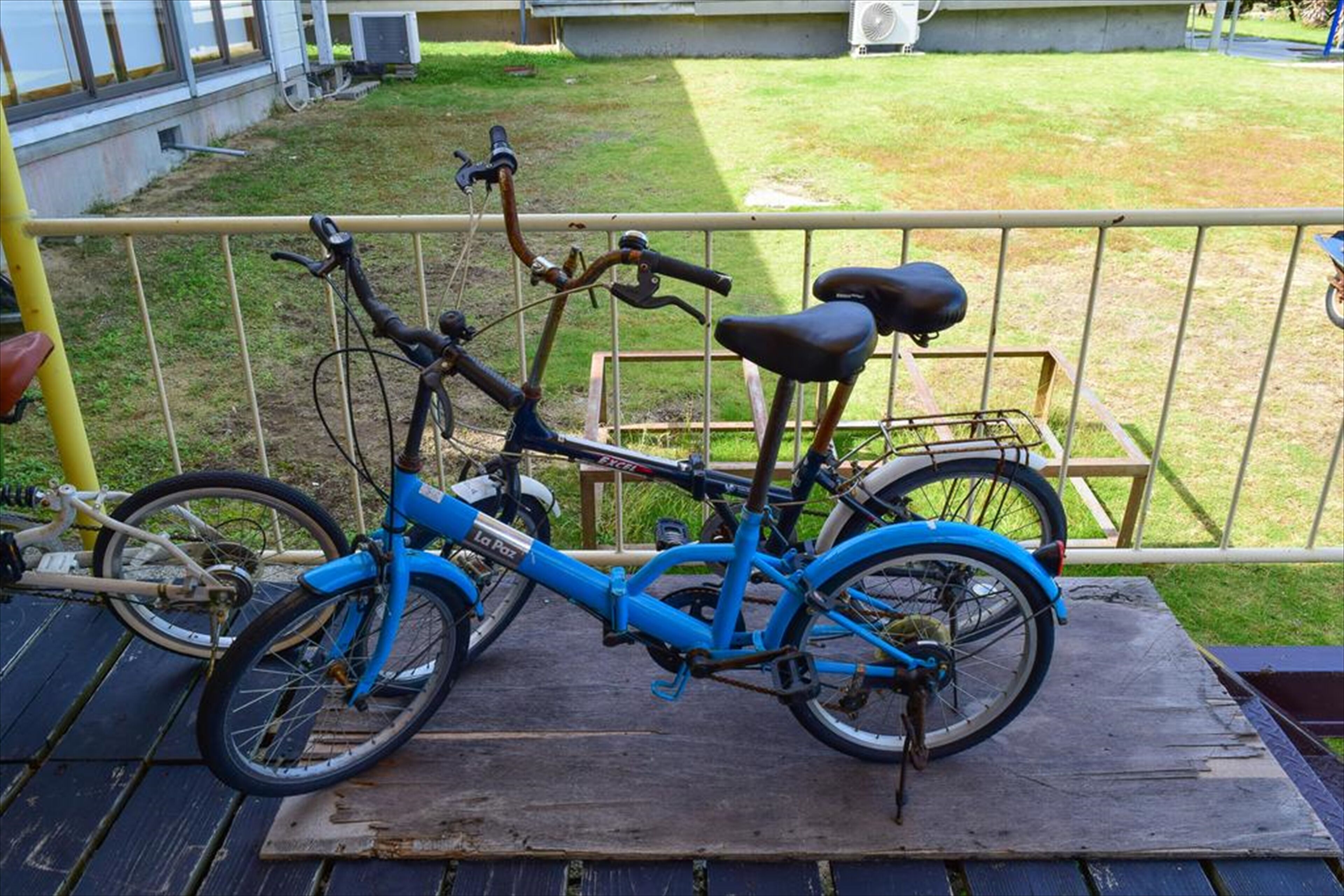 A blue bicycle parked on a wooden platform with a metal railing in the background.
