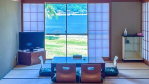 A room with tatami mat flooring, a low table with cushions, a television on a cabinet, and a view of the sea through shoji screens. - Seatiger Island In Shodoshima (Shodoshima)