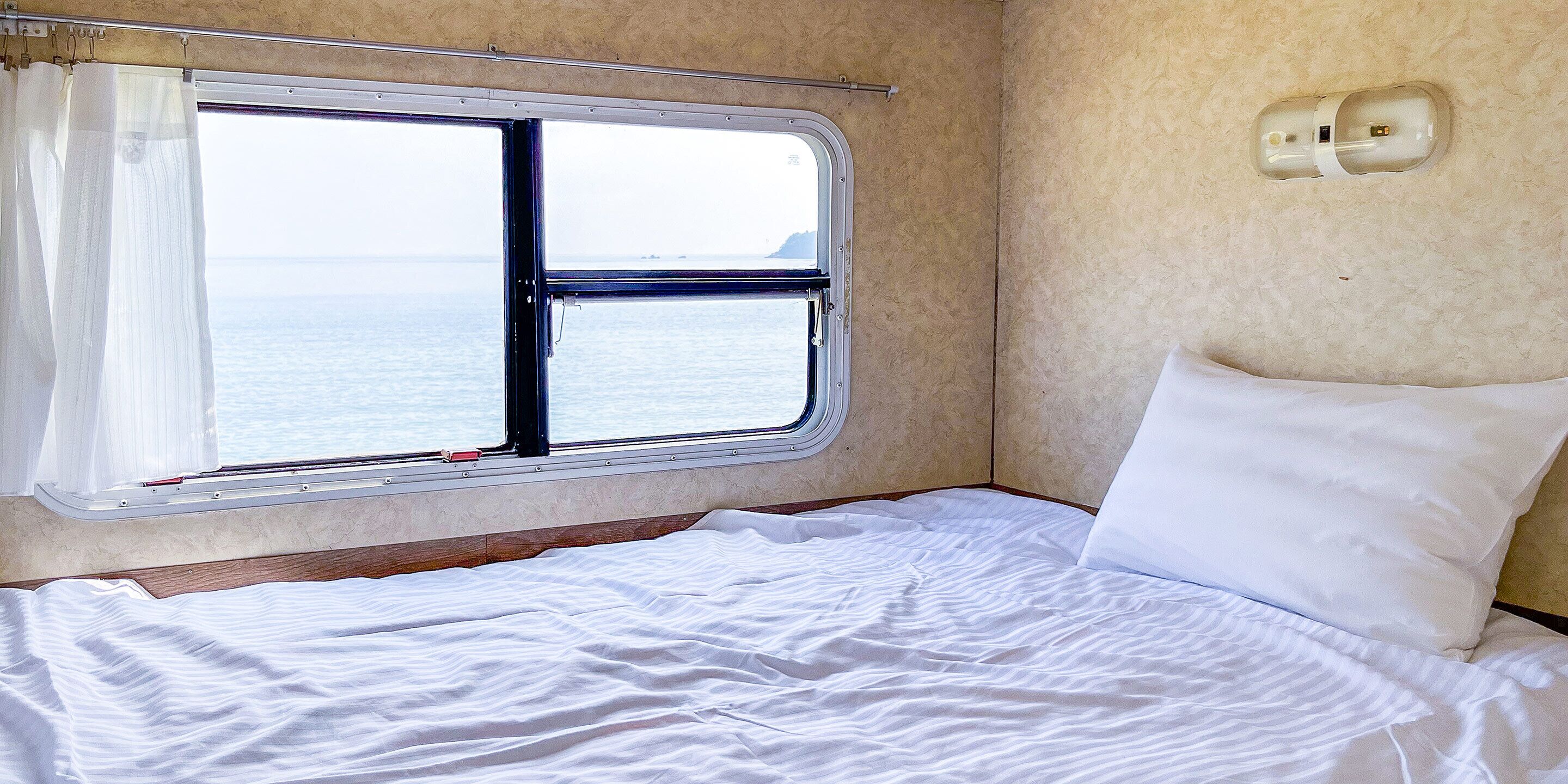 A bed with white bedding and a window with a view of the sea.