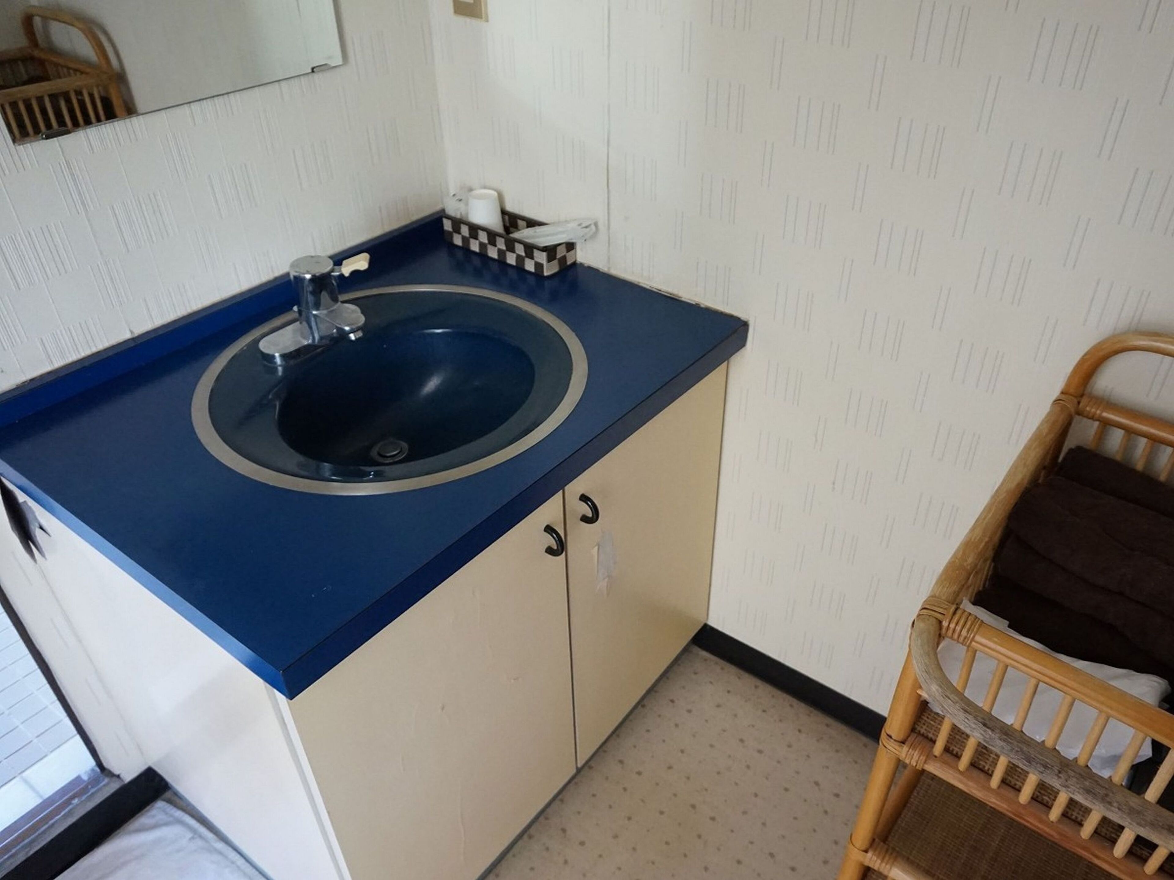 A bathroom with a blue sink, a mirror, and a wicker chair.