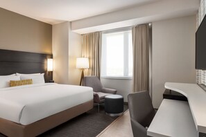 A hotel room with a large bed, a desk, a chair, a lamp, and a window with curtains. - Residence Inn by Marriott New York JFK Airport (Jamaica)