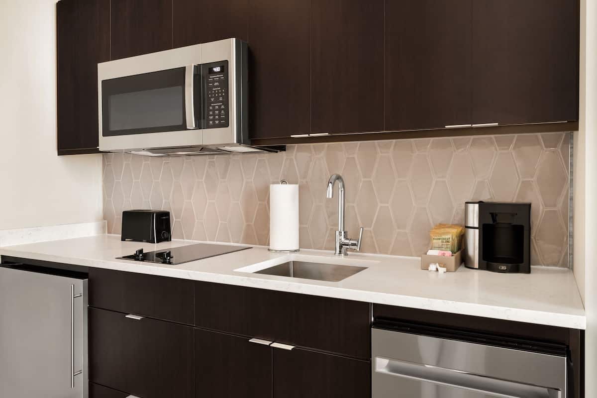A modern kitchen with dark wood cabinets, a stainless steel microwave, a sink, and a coffee maker.