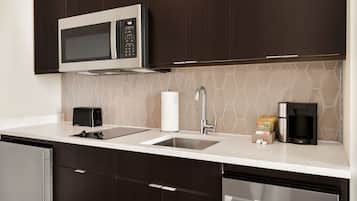 Una cocina moderna con armarios de madera oscura, un microondas de acero inoxidable, un lavabo y una cafetera.