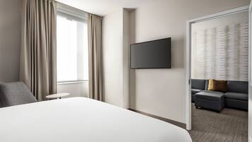 A modern hotel room with a large bed, a flat-screen TV mounted on the wall, a sofa, and a small table.