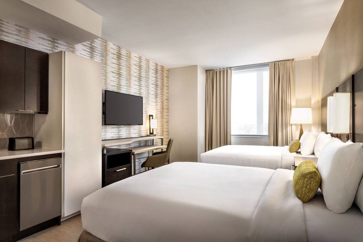 A hotel room with two beds, a desk with a chair, a television, and a window with curtains.