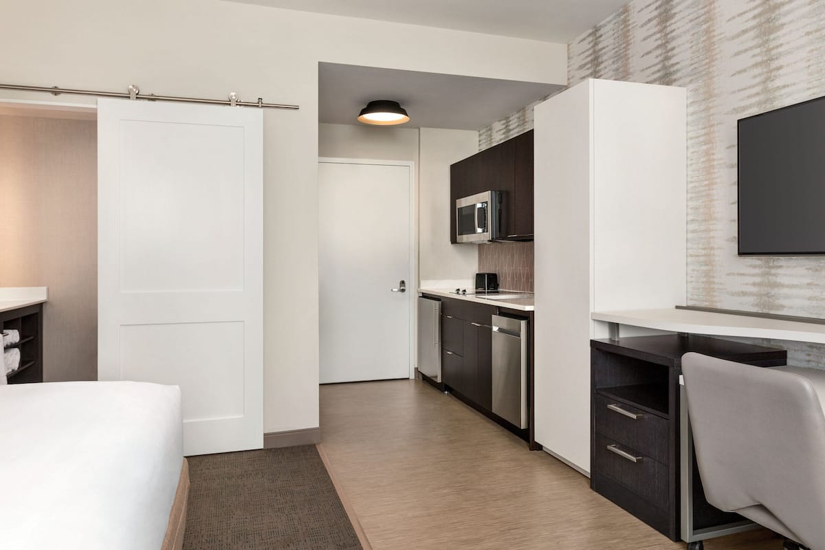 A modern hotel room with a bed, a desk, a microwave, and a TV.