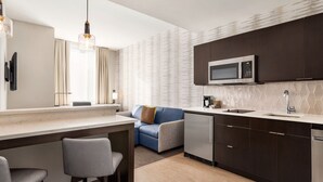 Una cocina moderna con armarios oscuros, un microondas y un lavamanos. Hay una zona de bar con taburetes y un ventanal con cortinas.