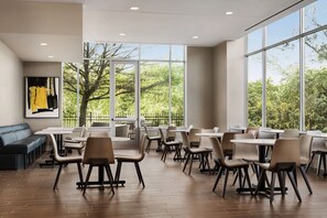 Un vaste espace dédié à la salle à manger, doté de grandes fenêtres, d’un plancher en bois et d’un assortiment de tables et de chaises.