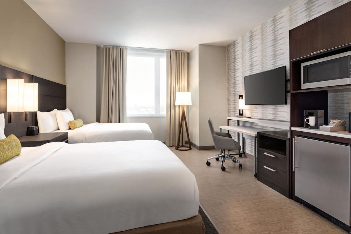 A hotel room with two beds, a desk with a computer, a flat-screen TV, a microwave, and a refrigerator.