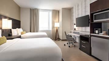 A hotel room with two beds, a desk with a computer, a flat-screen TV, a microwave, and a refrigerator.