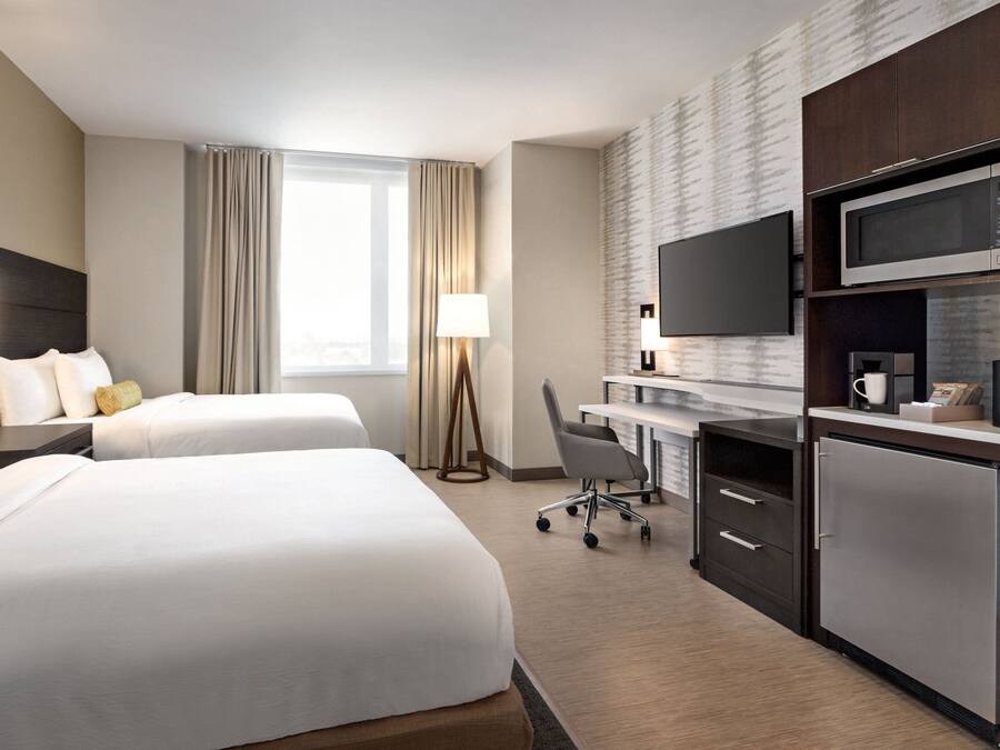A hotel room with two beds, a desk with a computer, a flat-screen TV, a microwave, and a refrigerator.