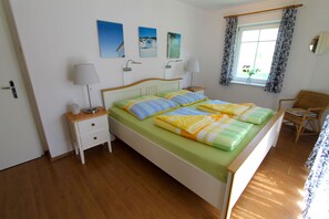 Ein Schlafzimmer mit einem Bett, Nachttischen, einem Sessel und einem Fenster mit Vorhängen.