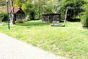 Ein Rasen mit einer Holzbank, einem kleinen Schuppen und einem Haus mit rotem Dach.