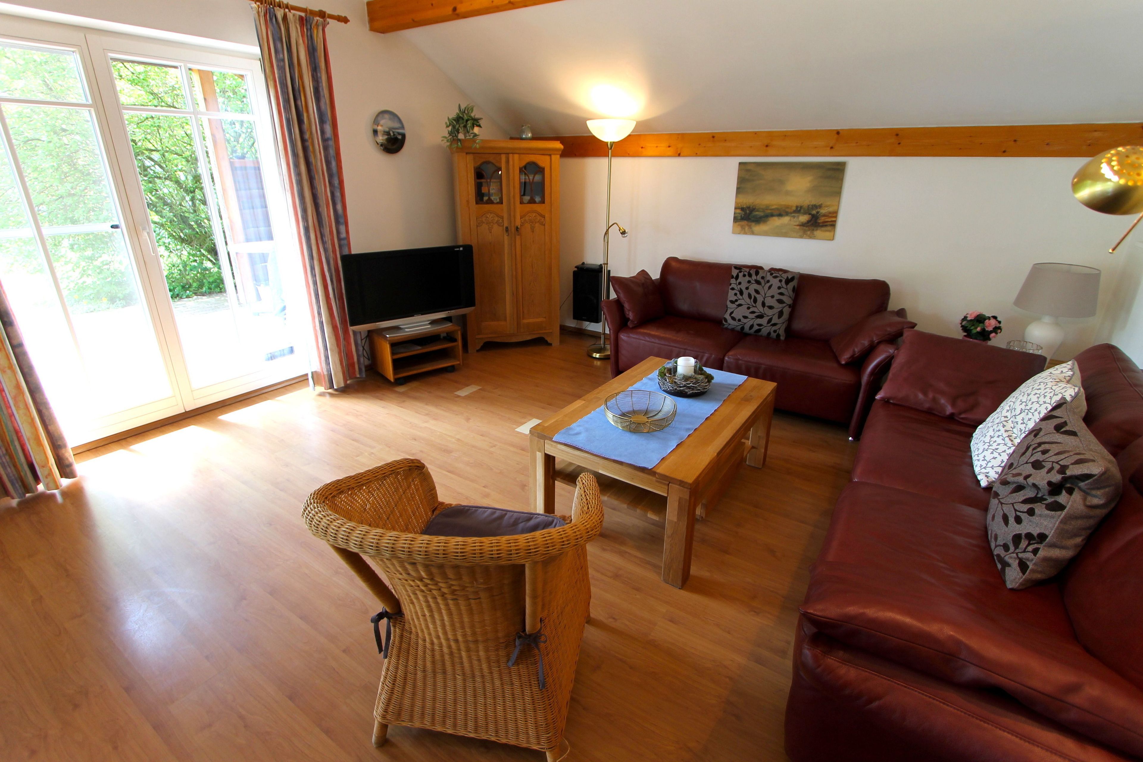 A living room with a wooden floor, a brown leather sofa, a wicker chair, a wooden coffee table, and a television.
