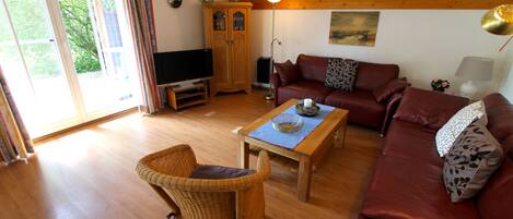 A living room with a wooden floor, a brown leather sofa, a wicker chair, a wooden coffee table, and a television.