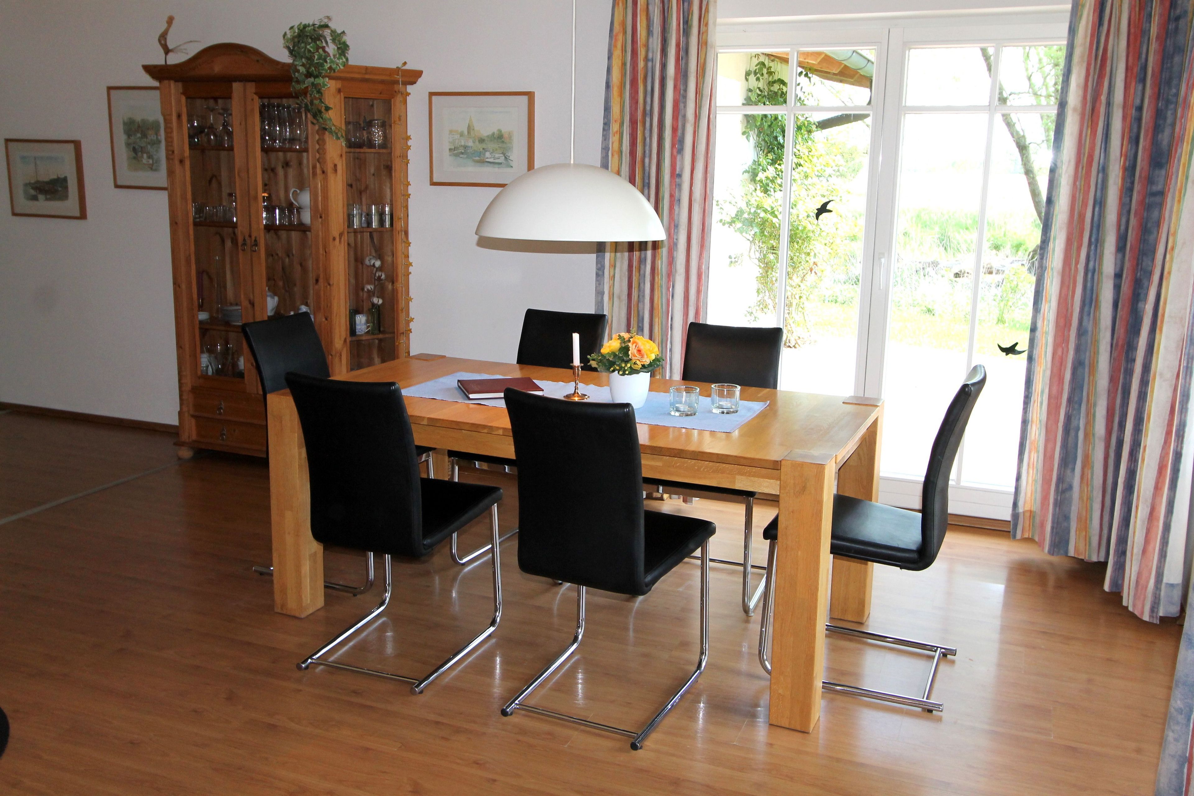 Un comedor con mesa de madera, sillas negras, una alacena con puertas de cristal y una ventana con cortinas.