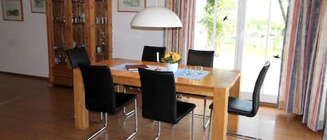 Un comedor con mesa de madera, sillas negras, una alacena con puertas de cristal y una ventana con cortinas.