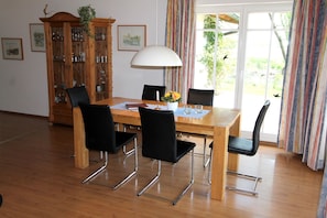 A dining area with a wooden table, black chairs, a cabinet with glass doors, and a window with curtains.