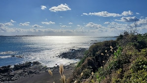 Paisagem costeira com linha de costa rochosa, céu claro e o sol refletindo na água.