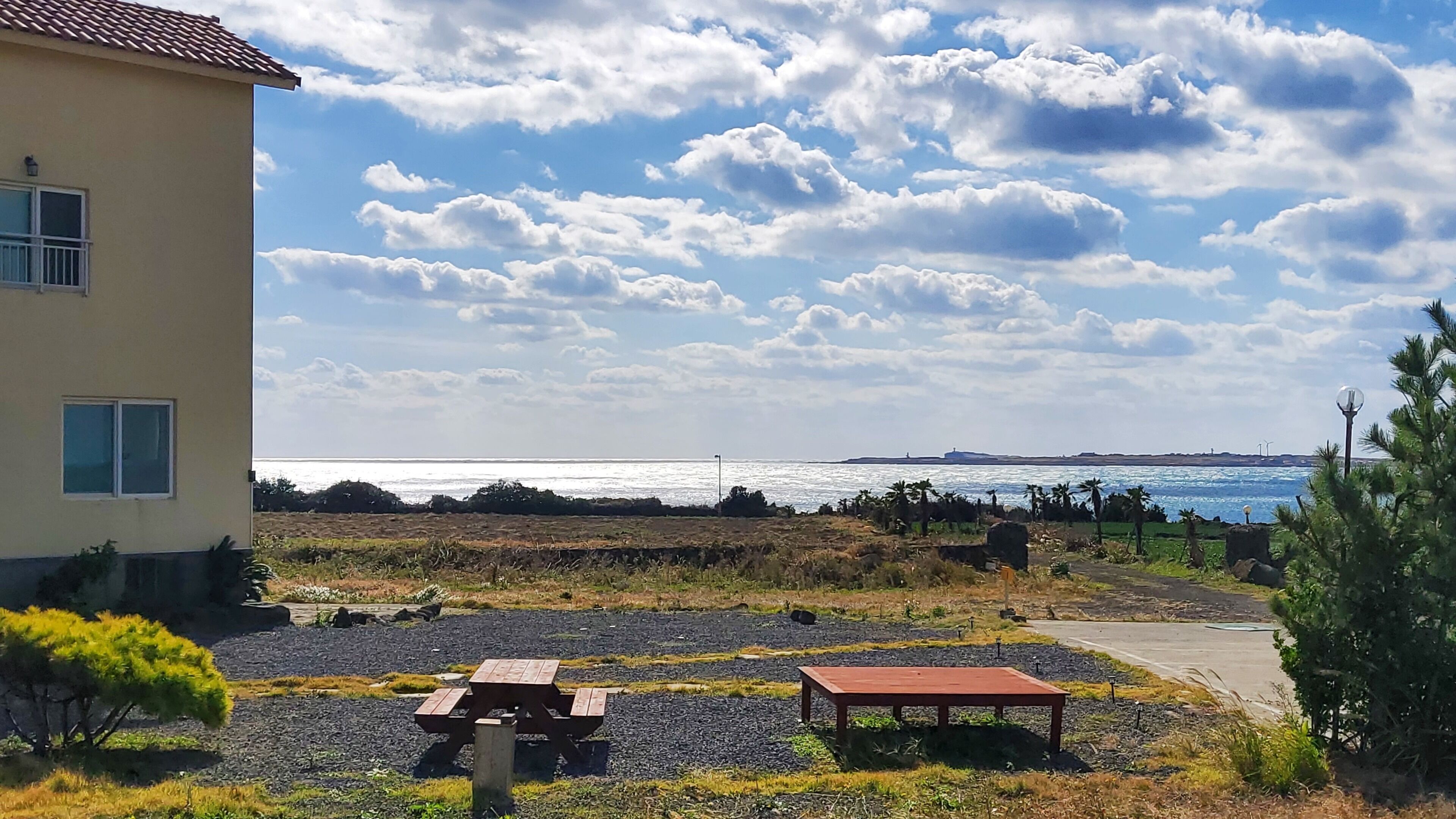 Une propriété située sur la côte, dotée d’un patio avec des tables de pique-nique, d’un petit bâtiment avec un toit en tuiles et d’une vue sur la mer.