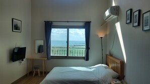 Quarto de hotel com cama, escrivaninha, televisão, janela com vista para o mar e ar condicionado.