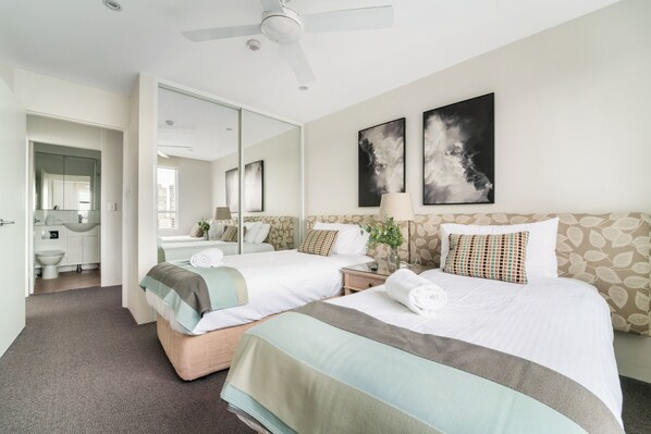 A hotel room with two beds, a large mirror, a ceiling fan, and artwork on the walls. - Harbourside 76 (McMahons Point)