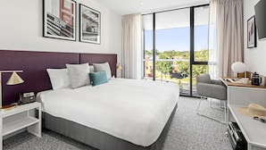 A modern hotel room with a large bed, a desk with a chair, a TV, and a view of the outdoors. - Quest Ballarat Station (Soldiers Hill)