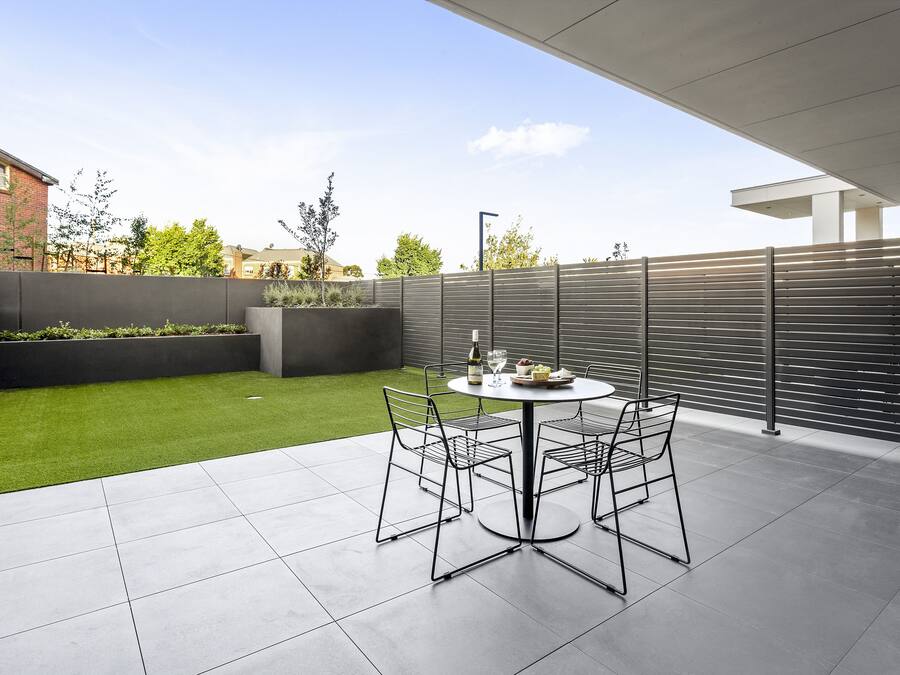 A patio with a round table and chairs, a small lawn, and a grey fence.