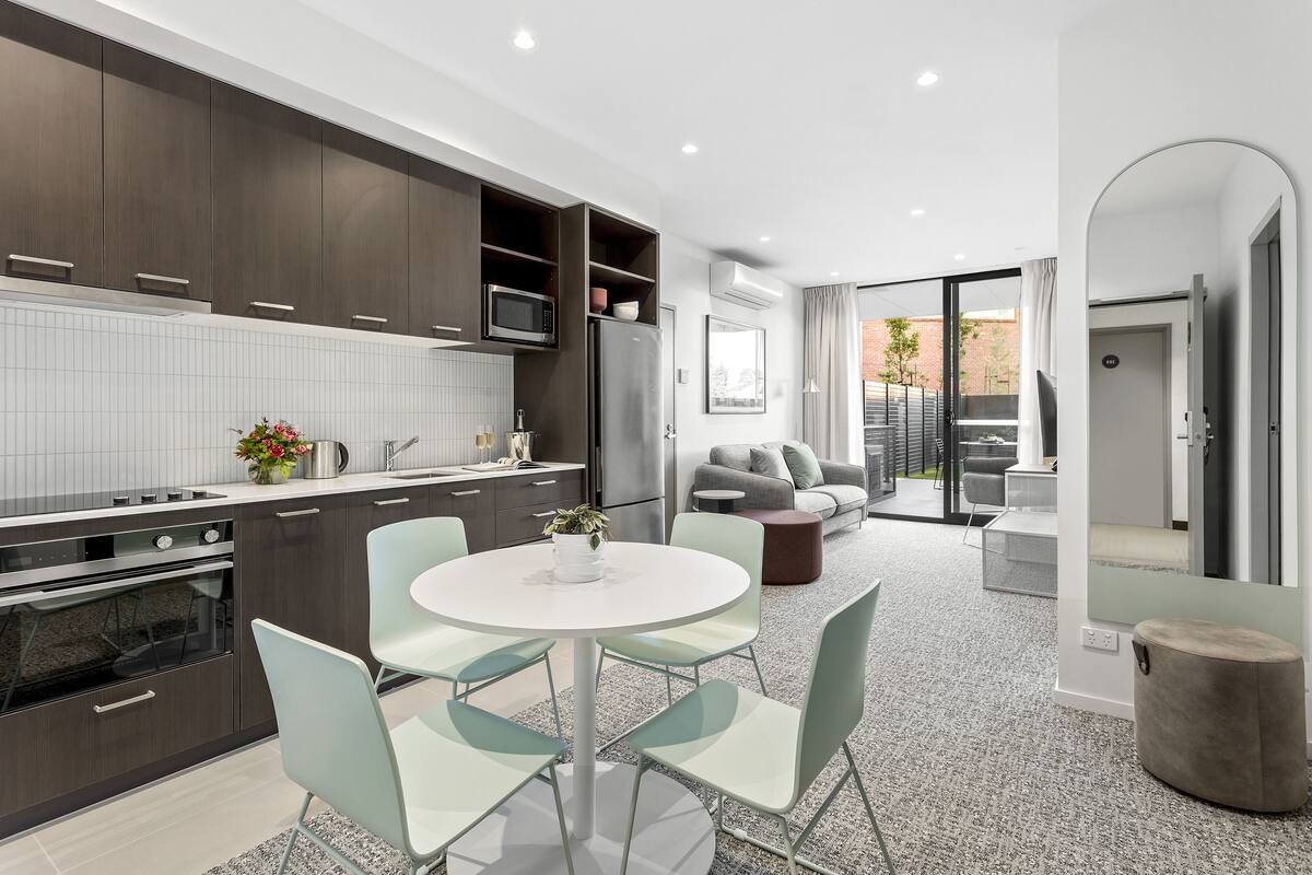 A modern kitchen with dark cabinets, a white countertop, and a round dining table with chairs.