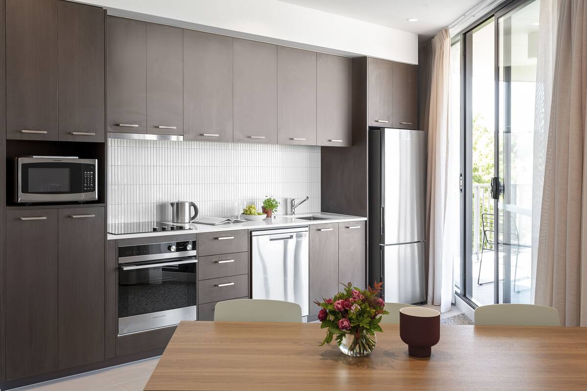 A modern kitchen with grey cabinets, stainless steel appliances, and a wooden dining table with a vase of flowers.