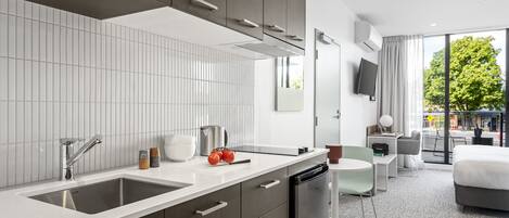 A modern hotel room with a kitchen area, a dining table, and a large bed.