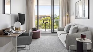 A modern hotel room with a large window, a sofa, a desk with a laptop, a chair, and a small table with a lamp. - Quest Ballarat Station (Soldiers Hill)