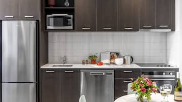 A modern kitchen with stainless steel appliances, dark wooden cabinets, a white tiled backsplash, and a dining area with a table set for two.