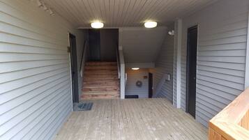 A wooden staircase leading to a second floor with a wooden deck and a light fixture above.