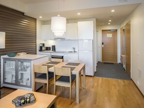 Cocina compacta con electrodomésticos modernos, zona de comedor con mesa y sillas, y un aparador de vidrio con vajilla.
