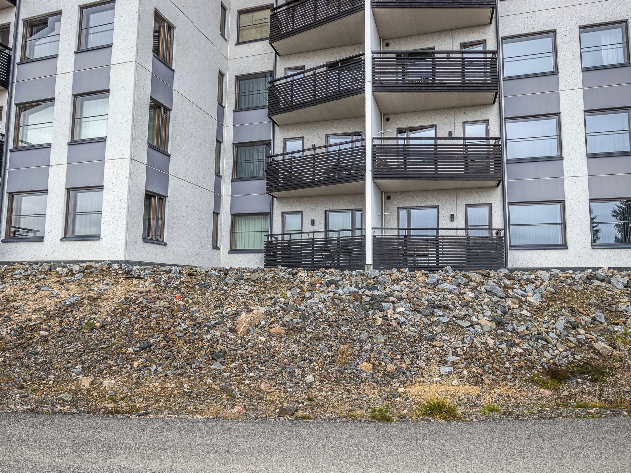 A multi-story building with balconies, a stone retaining wall, and a paved ground.