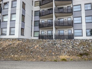 A multi-story building with balconies, a stone retaining wall, and a paved ground.