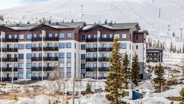 Un hôtel à plusieurs étages doté de balcons, situé dans une région montagneuse enneigée, avec des pistes de ski en arrière-plan.