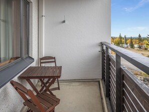 Un balcon avec une table et des chaises en bois, une fenêtre et une vue sur des arbres et un véhicule.