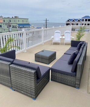 Ein Balkon mit Korbmöbeln, einem kleinen Tisch und zwei weißen Stühlen.