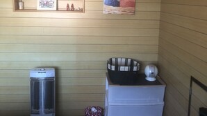 A room with wooden panel walls, a radiator, a white chest of drawers, a striped basket, and a framed picture of a cat. - Minshuku Tomato House (Tamura)